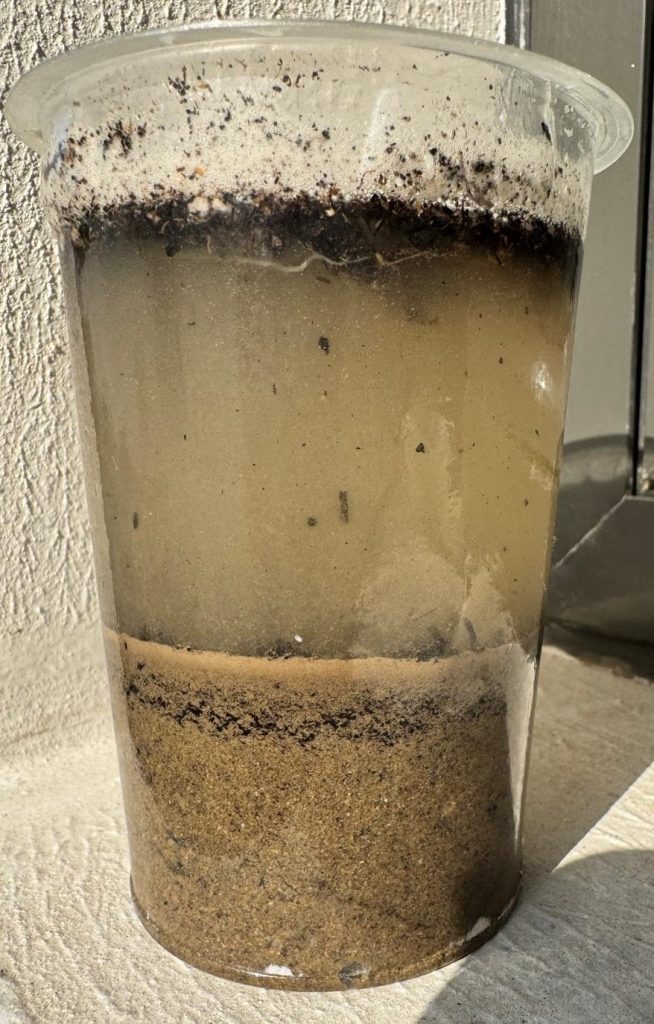 Jar filled with soil and water showing the levels of sand, silt, clay and loamy soil